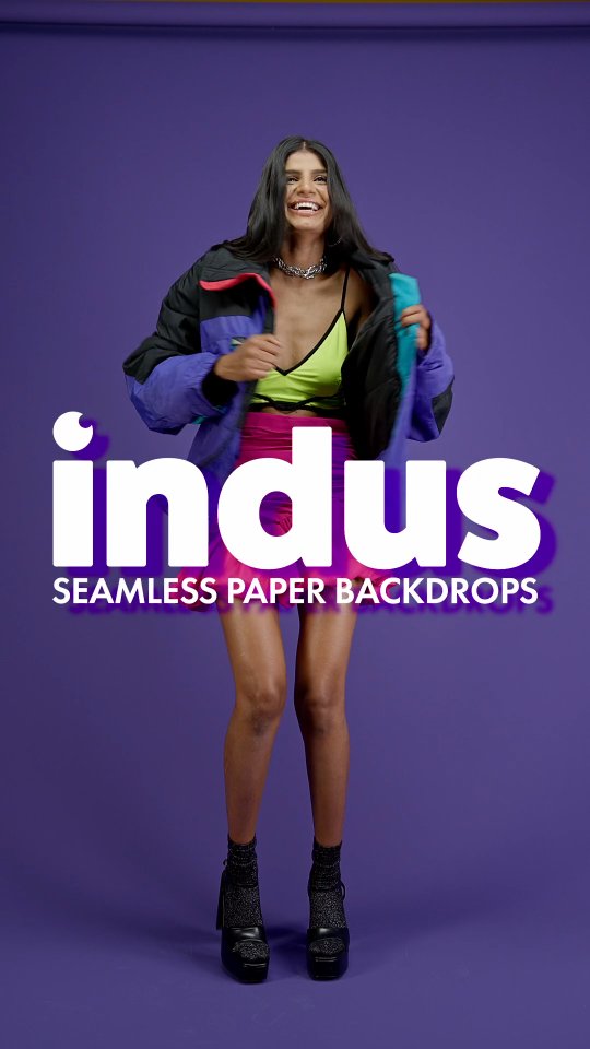 Model wearing neon outfit posing in front of a purple backdrop with the large 'indus' logo and 'Seamless Paper Backdrops' text.