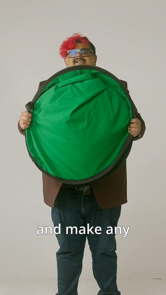 Person standing and holding a large green circular prop in front of their torso, partially covering their body; text overlay at bottom reads “and make any.”