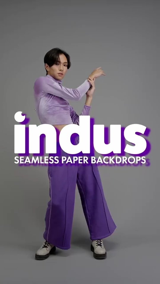 Model wearing a lavender cropped top and purple wide-leg pants poses against a gray backdrop with bold white text reading 'indus' and 'SEAMLESS PAPER BACKDROPS' overlaid.
