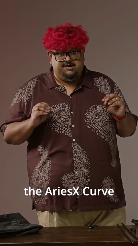 Man with bright red curly hair and glasses gestures while wearing a brown paisley shirt, with text 'the AriesX Curve' overlaid.