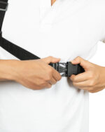 Person in a white polo shirt adjusting a black shoulder strap buckle across the chest.