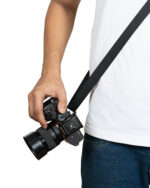 Hand gripping a Sony camera with a black strap, held at hip level against a white background