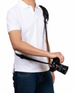 Person in a white polo holds a DSLR camera by its strap.