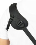 Close-up of a black shoulder strap with buckle on a white shirt, showing a tactical bag strap over the shoulder.