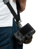 Person in denim overalls with a black camera strap, holding a DSLR camera at their side.