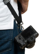DSLR camera hanging on a black strap at the wearer's hip with denim jeans visible atop a white shirt