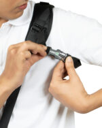 Close-up of a person adjusting a black backpack strap with a buckle on their shoulder on a white shirt