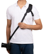 Person in a white polo shirt with a black diagonal camera strap across their chest, holding a DSLR at the hip area.