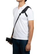 Person in a white polo shirt wearing a black camera strap over the shoulder with a camera hanging at the hip.