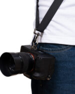 Sony DSLR camera with a black strap hanging from a person wearing a white shirt and blue jeans