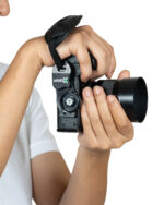 Close-up of a person gripping a black camera with a large lens and wrist strap against a white background.