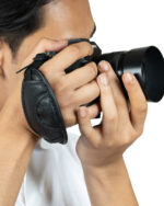 Person holding a black DSLR camera up to their eye, ready to take a photo, with a camera strap visible on the side.