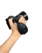 Close-up of a hand gripping a black DSLR camera with a large lens hood, set against a white background.