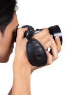 Person holding a black DSLR up to their eye, looking through the viewfinder with a camera strap around the wrist.