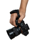 Close-up of a hand gripping a black Sony camera with a strap attached to the top handle