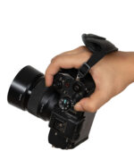 Close-up of a hand gripping a black DSLR camera with a strap across the back of the hand