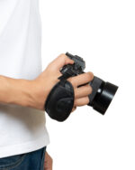 Person wearing a white shirt and jeans holding a black DSLR camera with a neck strap in front of them