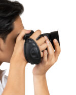 Close-up of a person holding a black camera to their eye, ready to take a photo, against a white background.
